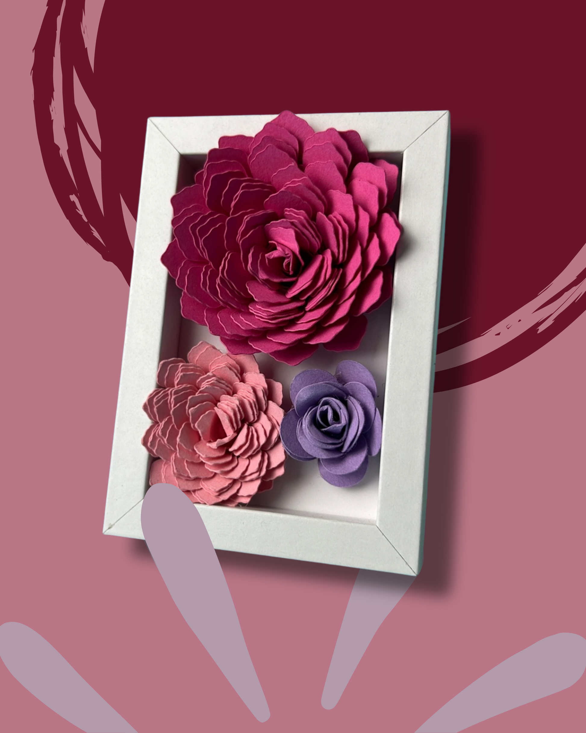 Kleiner weißer Bilderrahmen mit drei Blumen in Pink,lila und rosa vor weißem Hintergrund.