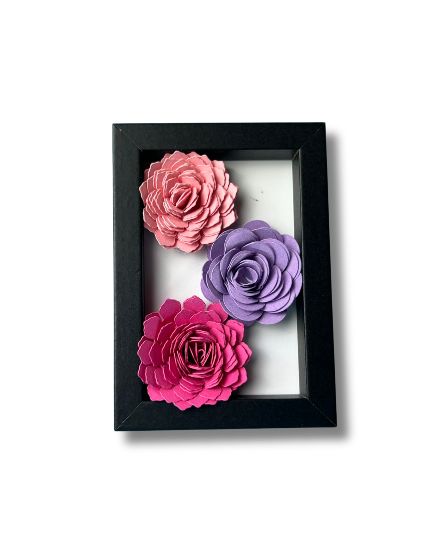 Kleiner schwarzer Bilderrahmen mit drei Blumen in Pink,lila und rosa vor weißem Hintergrund.