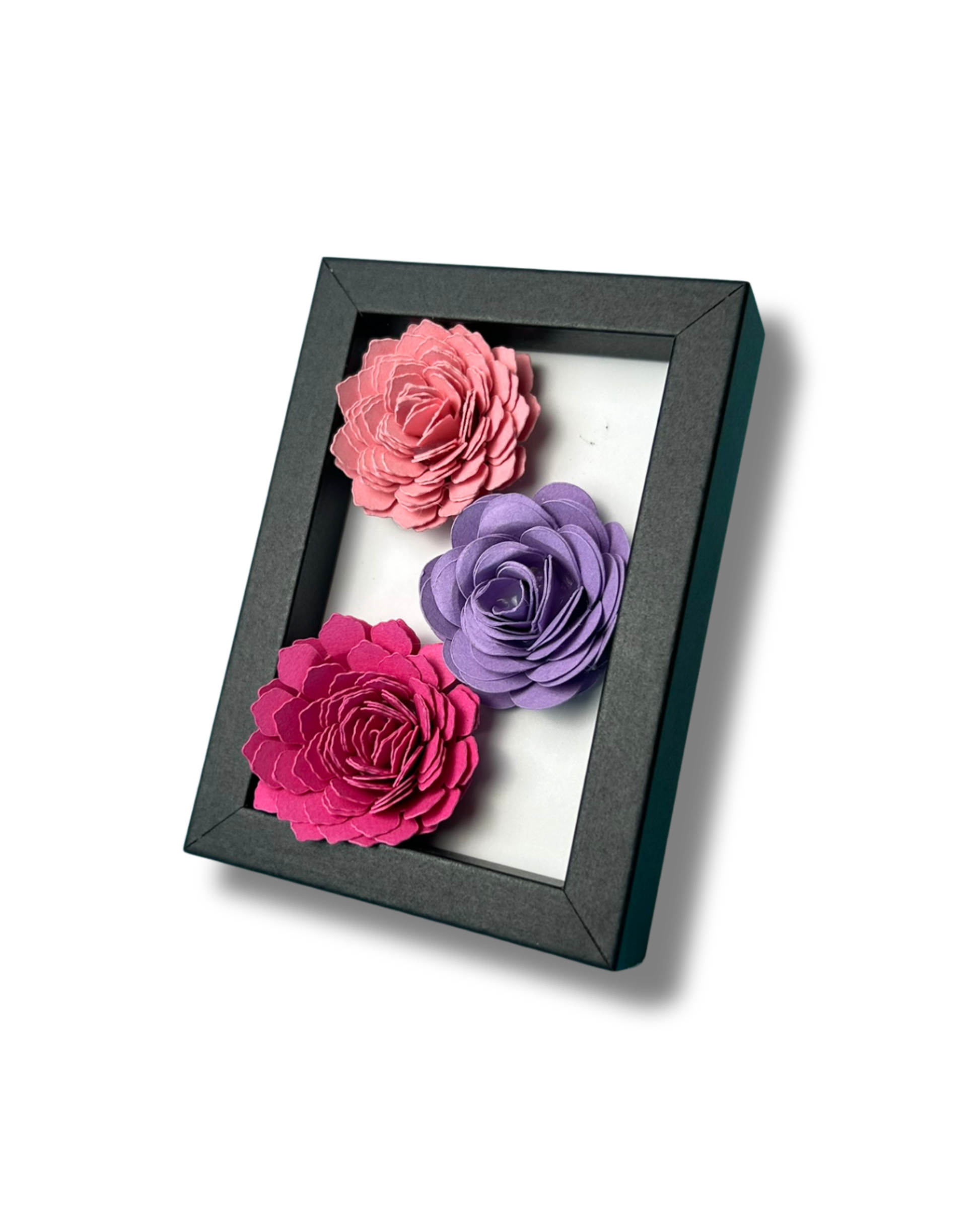 Kleiner schwarzer Bilderrahmen mit drei Blumen in Pink,lila und rosa vor weißem Hintergrund.