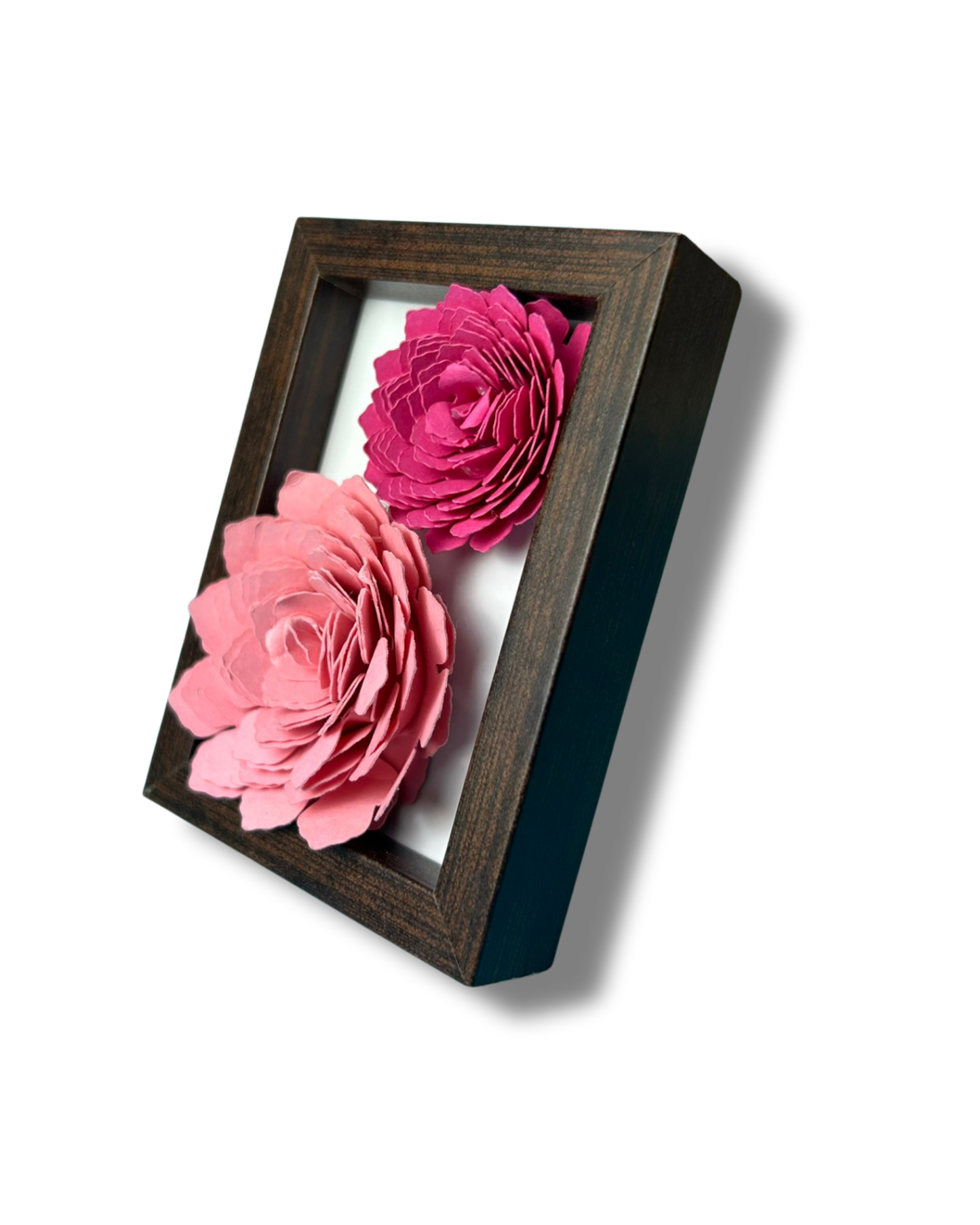 Kleiner dunkelbrauner Bilderrahmen mit zwei Blumen in Pink und rosa vor weißem Hintergrund.