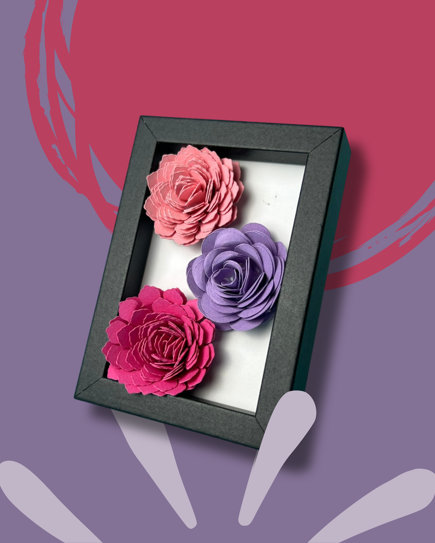 Kleiner schwarzer Bilderrahmen mit drei Blumen in Pink,lila und rosa vor weißem Hintergrund.