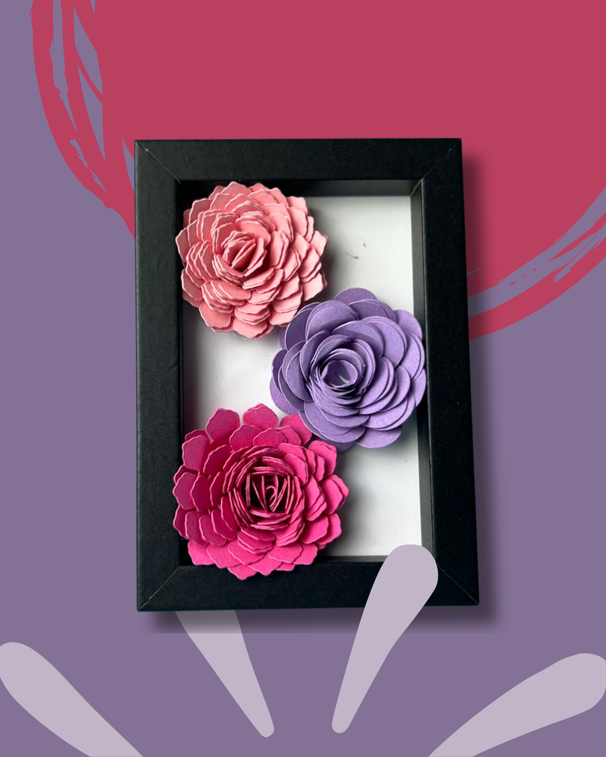 Kleiner schwarzer Bilderrahmen mit drei Blumen in Pink,lila und rosa vor weißem Hintergrund.