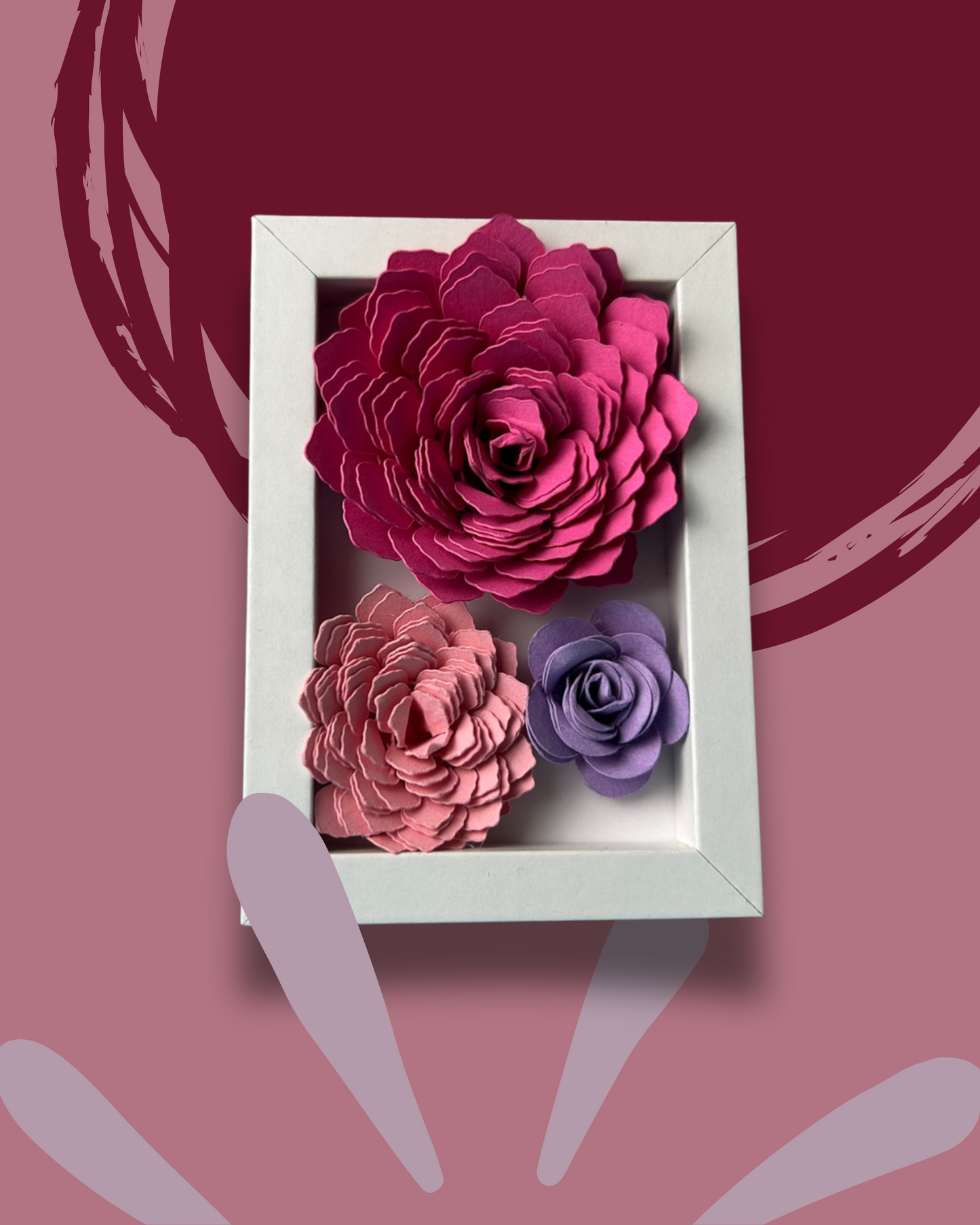 Kleiner weißer Bilderrahmen mit drei Blumen in Pink,lila und rosa vor weißem Hintergrund.